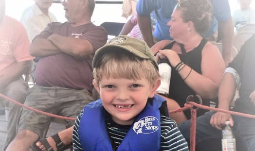 A young angler in a life jacket smiling at a kids’ fishing clinic